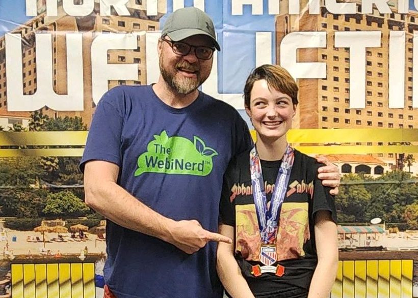 A picture of Joshua Jones with his daughter, Hazel at a power lifting tournament medal presentation.